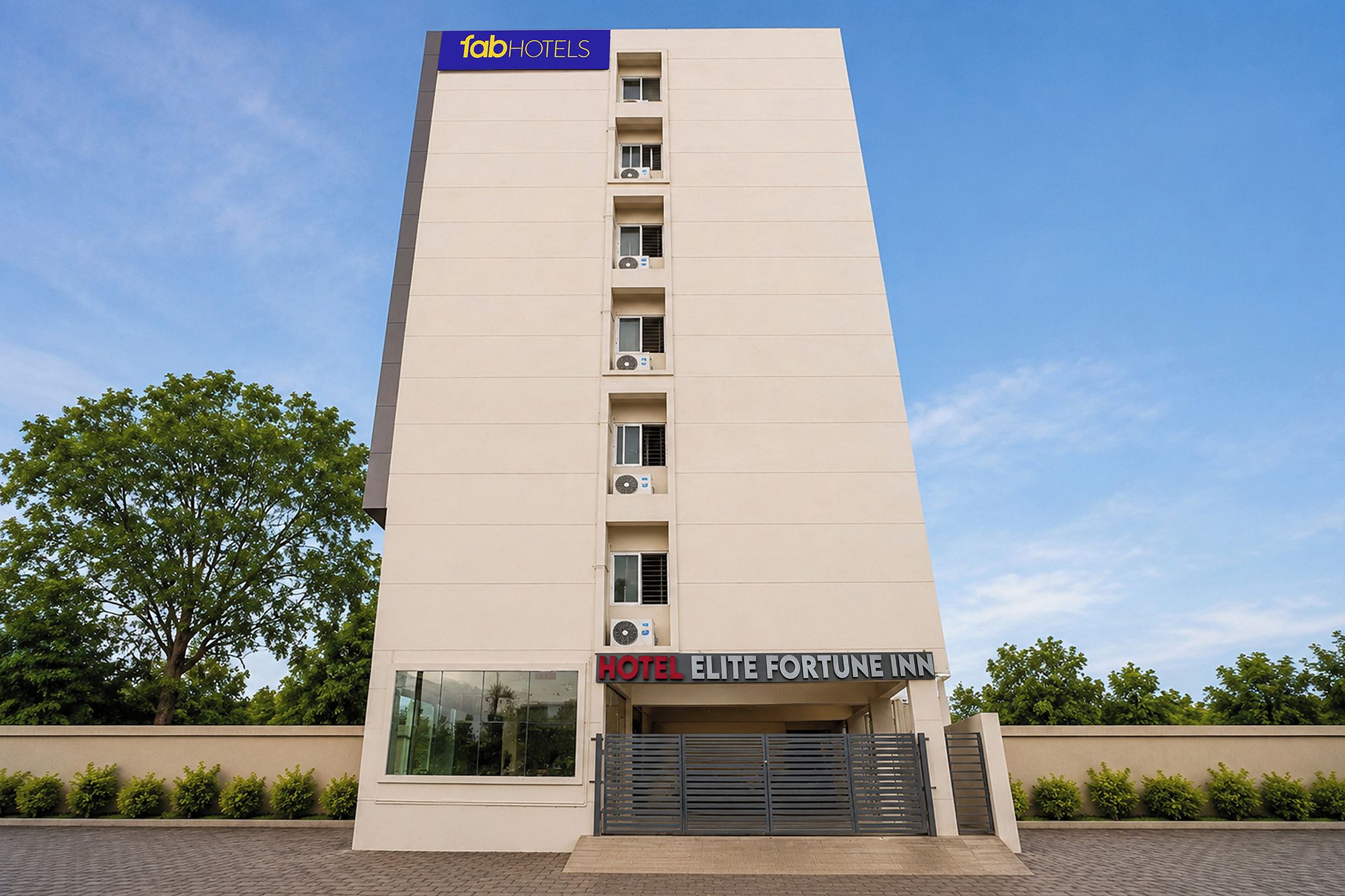 A tall, modern hotel building with a flat facade, multiple air conditioning units, and a prominent sign for 'HOTEL ELITE FORTUNE INN' at the bottom.