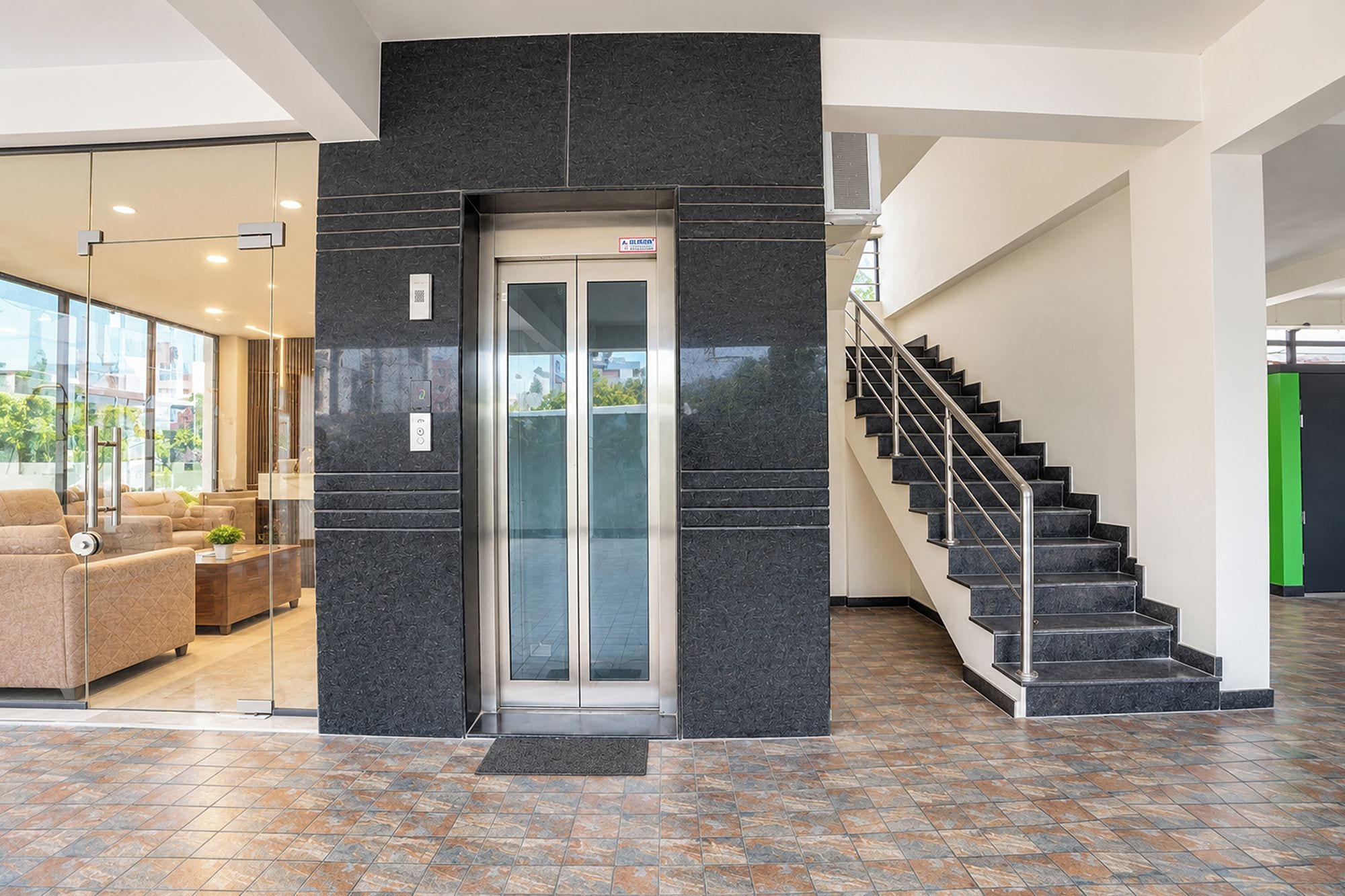 Un vestíbulo moderno con un ascensor de vidrio, una escalera y una zona de estar con sofás.