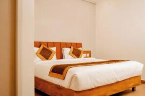 Cama de casal com cabeceira de madeira, roupa de cama branca e duas almofadas decorativas.