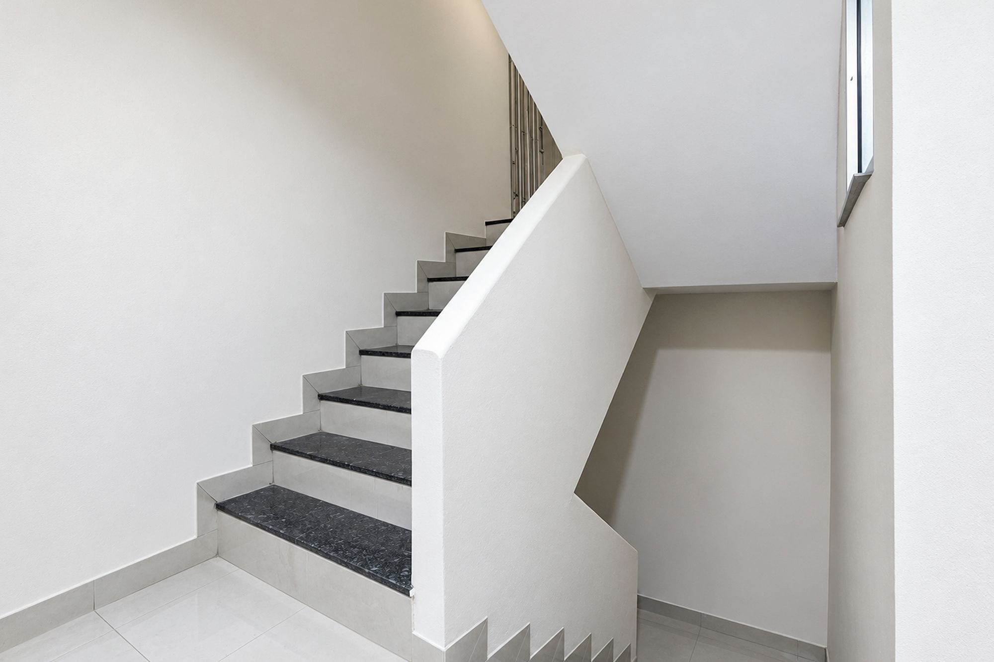 Una escalera con paredes blancas y escalones negros.