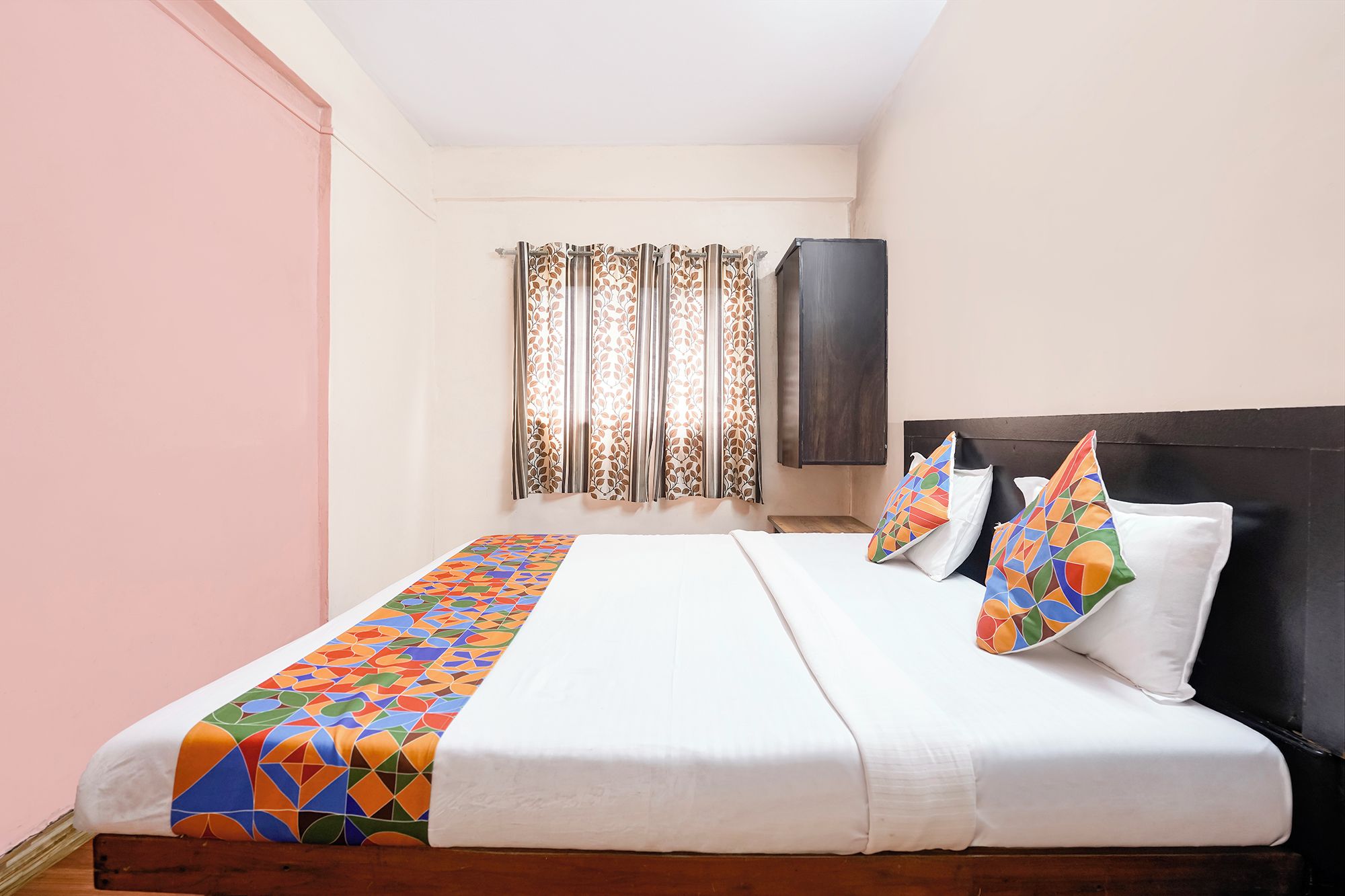 Una cama individual con una colcha estampada, un cabecero oscuro y almohadas decorativas.