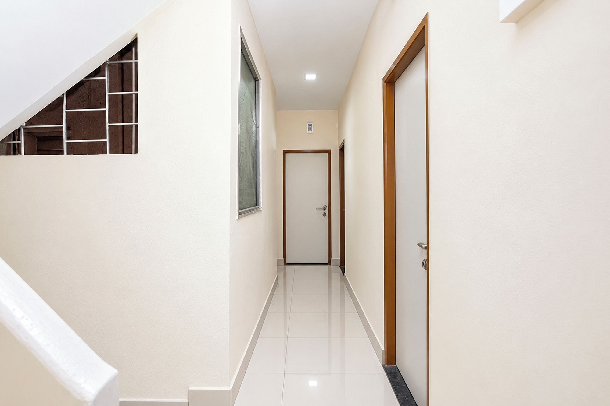 Un pasillo con una escalera a la izquierda, una puerta al final y una ventana a la derecha.