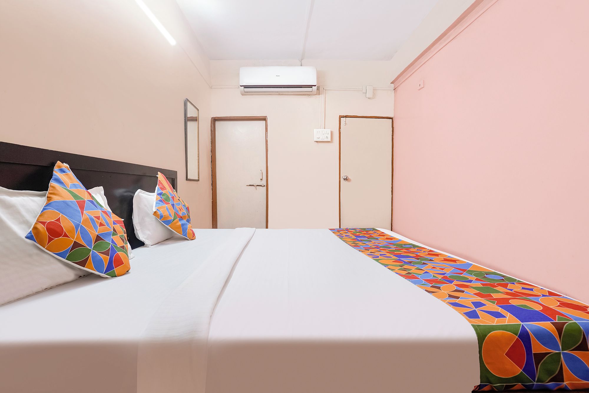 Habitación de hotel con cama, mesita de noche, unidad de aire acondicionado y una puerta.