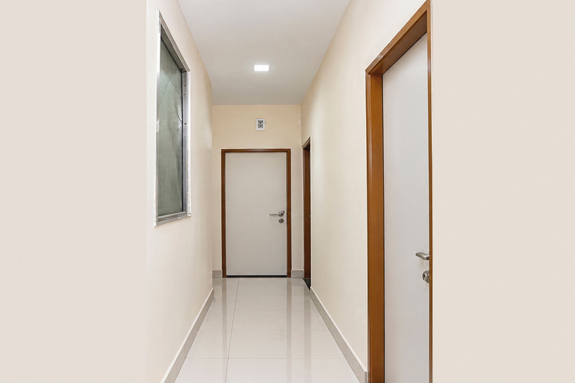 Un pasillo con una puerta al final, una ventana a la izquierda y un accesorio de iluminación en el techo.