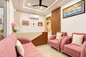 A reception area with a reception desk, a clock, and a painting on the wall. There are two pink sofas with cushions. - FabHotel Livora Stays (Lucknow)