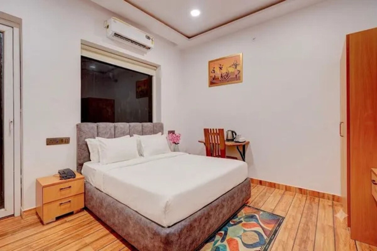 A bedroom with a bed, bedside table, chair, and an air conditioning unit.
