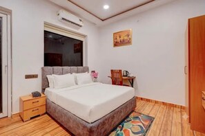 A bedroom with a bed, bedside table, chair, and an air conditioning unit. - FabHotel Livora Stays (Lucknow)