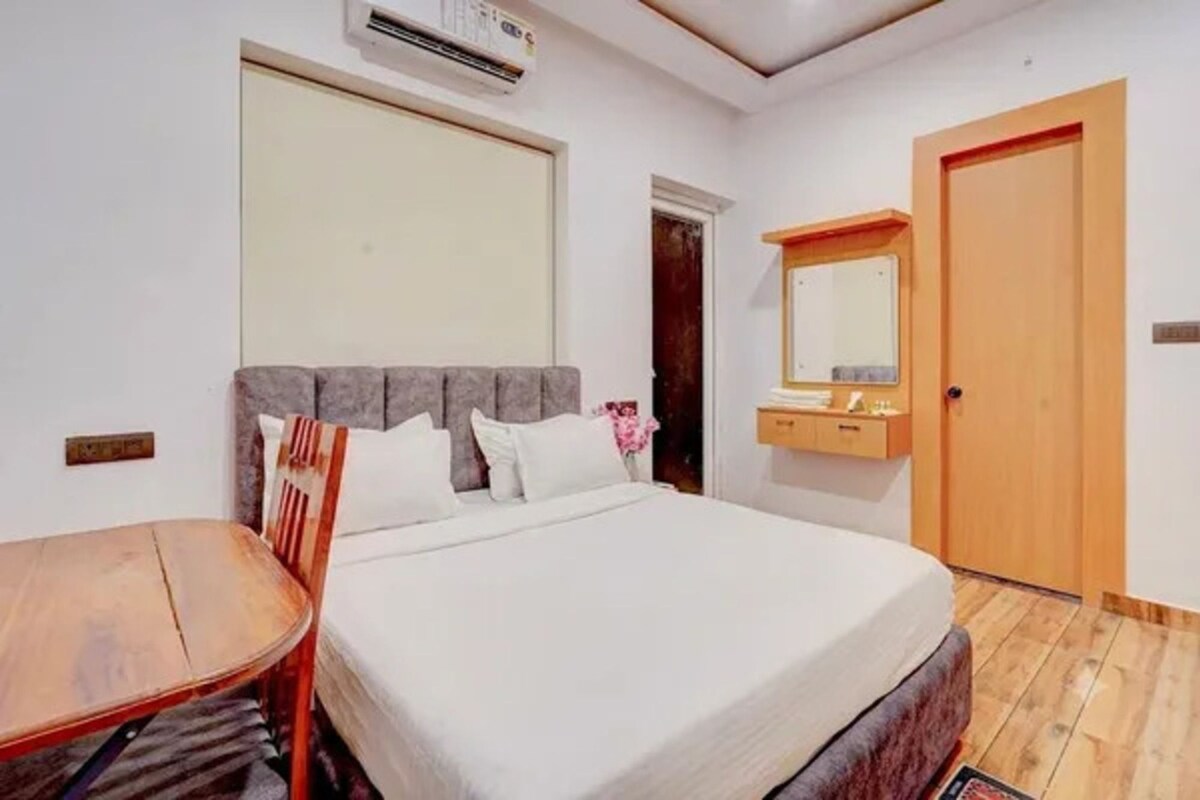 A bedroom with a bed, a bedside table, a mirror, and a door.