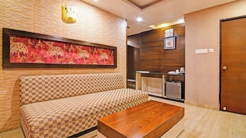 Quarto de hotel com sofá xadrez, mesa de centro de madeira, obra de arte na parede e armário de madeira com espelho.