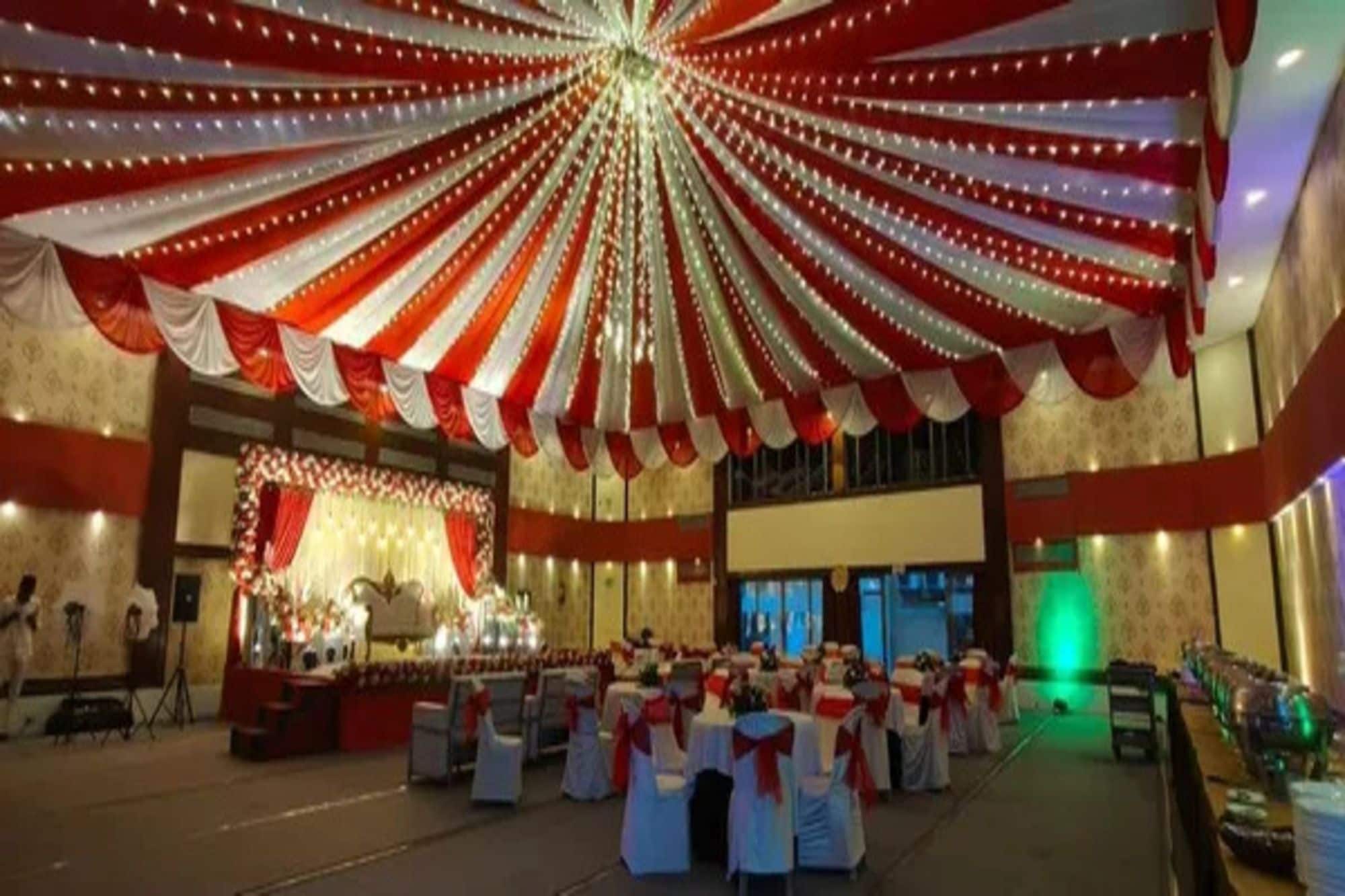 Un salón de banquetes con filas de mesas, cubiertas con tela roja y blanca, y un escenario con instrumentos musicales.