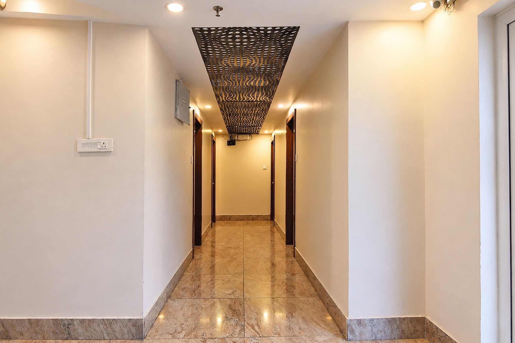 Un pasillo de hotel con techo estampado, suelo de mármol e iluminación empotrada.