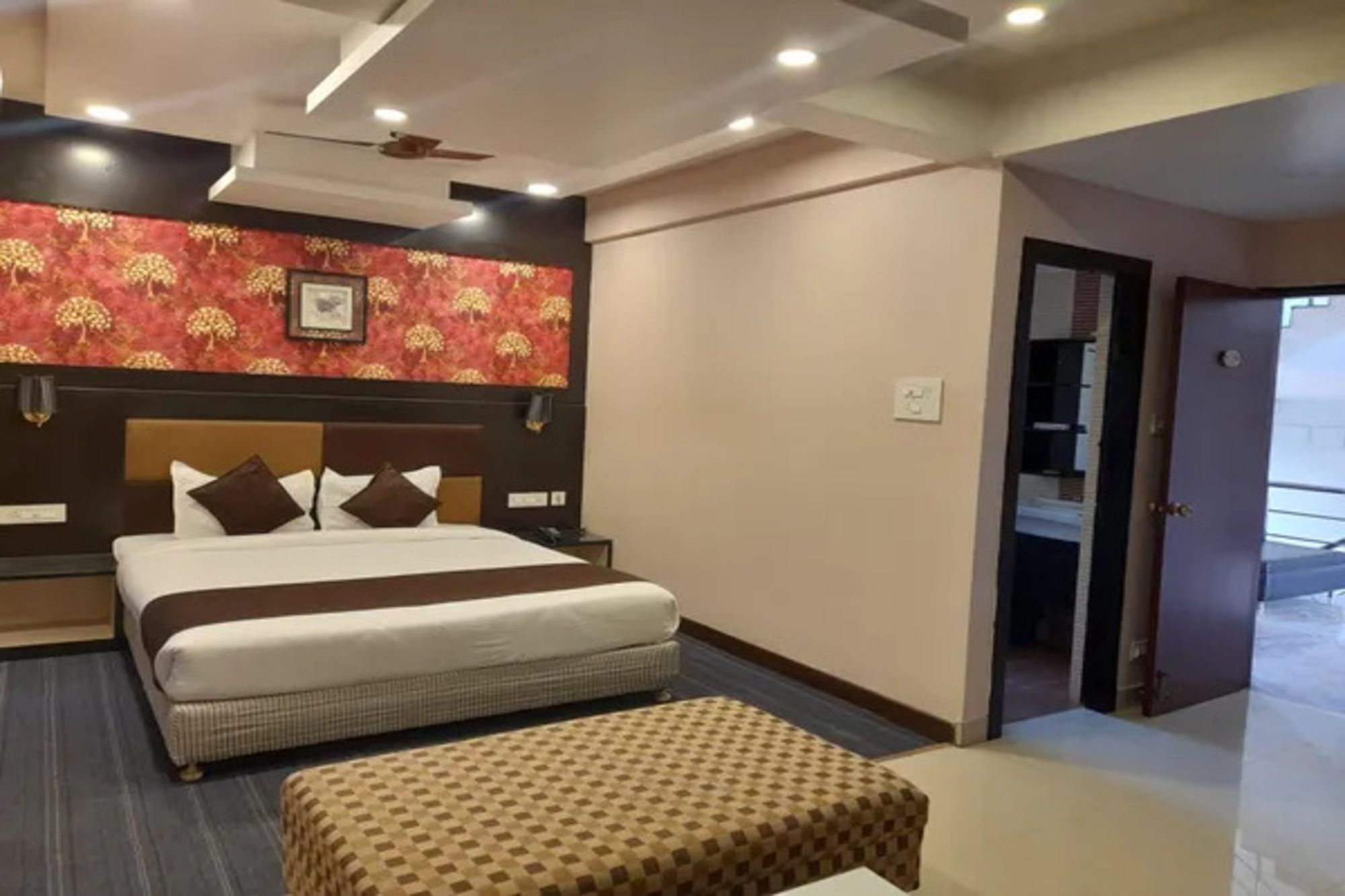 Una habitación de hotel con una cama, un banco, un ventilador de techo y una puerta que da a otra habitación.