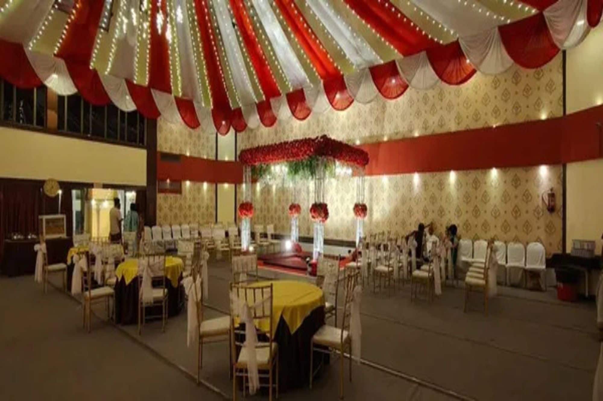 Un salón de banquetes con mesas redondas, sillas y un escenario decorado con flores.