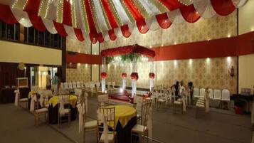 Un salón de banquetes con mesas redondas, sillas y un escenario decorado con flores.