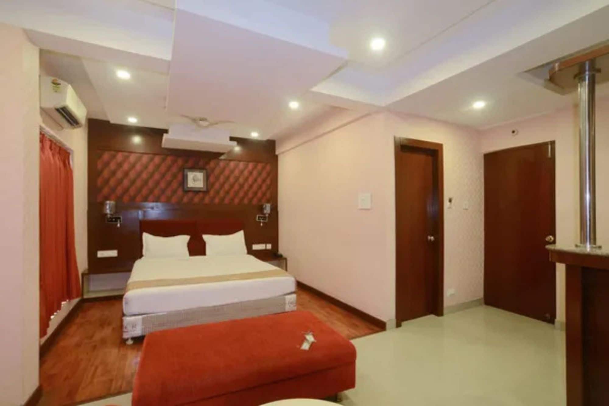 Una habitación de hotel con cama doble, un reposapiés rojo, un armario de madera y un ventilador de techo.