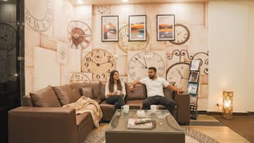 A lobby with a brown leather sofa, a glass coffee table, and a wall decorated with clocks and framed artwork.