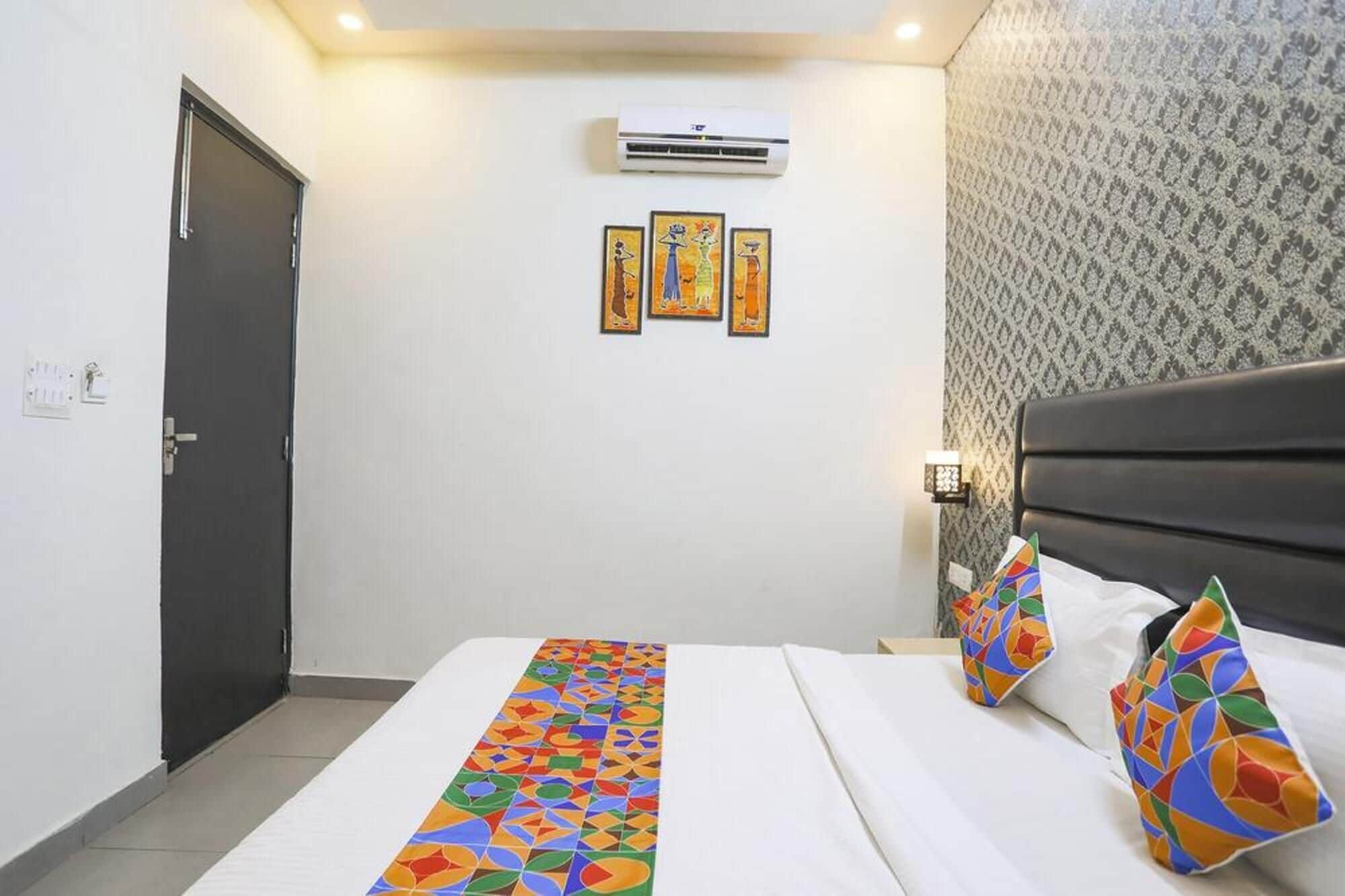 A hotel room with a bed, a bedside table, a wall-mounted air conditioner, and a door.