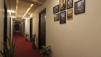 A hotel hallway with a red carpet, potted plants, and framed pictures on the walls.