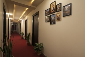 A hotel hallway with a red carpet, potted plants, and framed pictures on the walls. - FabHotel The Diamond (Noida)