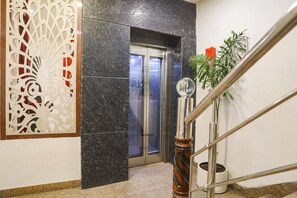 A hotel lobby with a marble wall, a decorative panel, a staircase with a metal railing, and a potted plant. - FabHotel The Diamond (Noida)