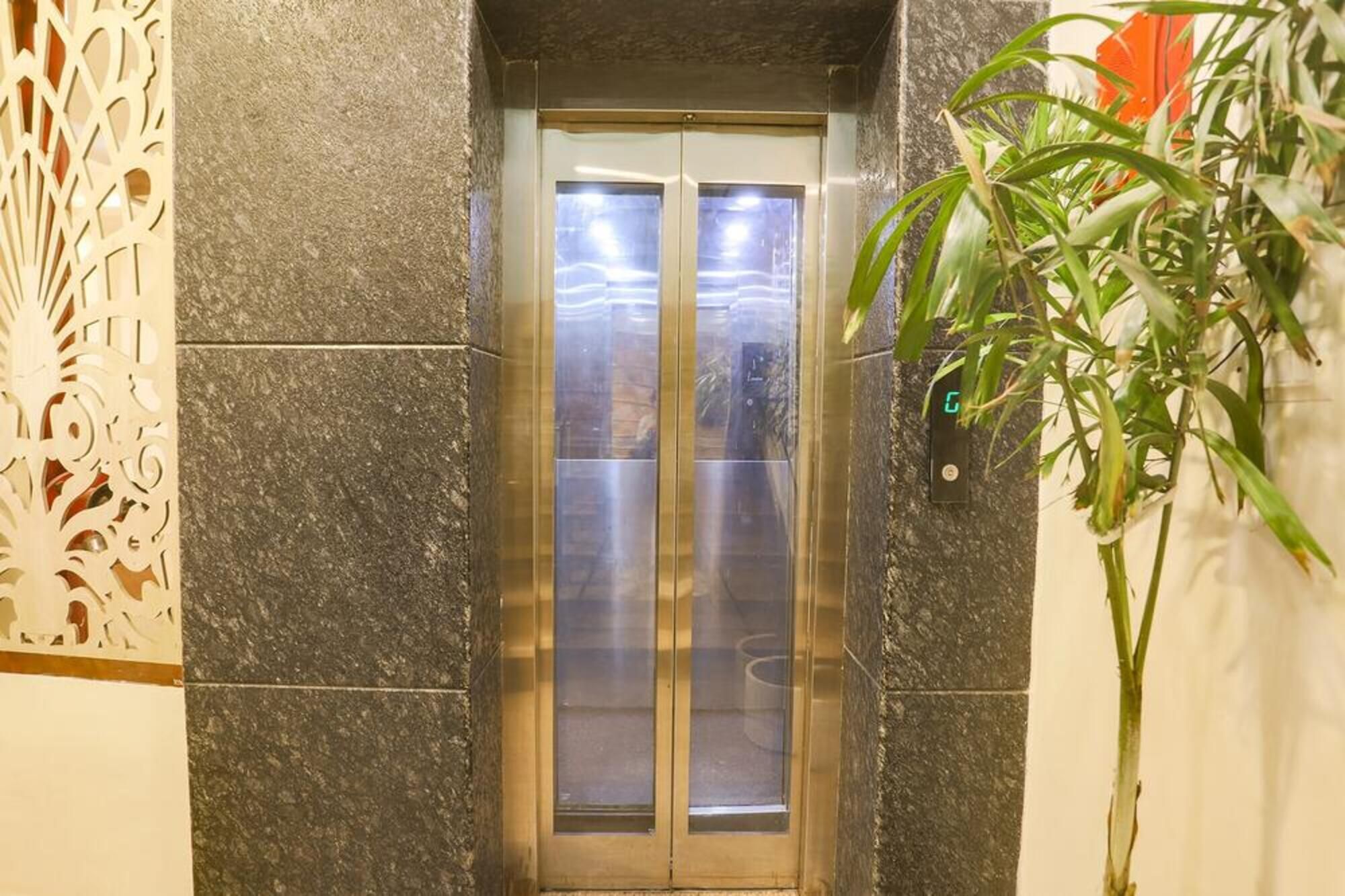 An elevator with a metallic interior and glass doors, surrounded by stone walls and a decorative panel.