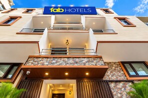 Fachada de hotel com um grande letreiro 'fab HOTELS', entrada em ladrilho de pedra e design moderno para a varanda.