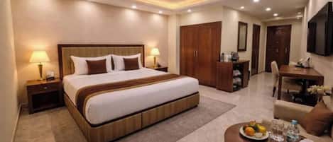 Habitación de hotel con una cama grande, lámparas de noche, un escritorio, una silla y una mesa de comedor con un plato de fruta.