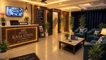 A hotel reception area with a reception desk, a television, and a seating area with sofas and a coffee table.