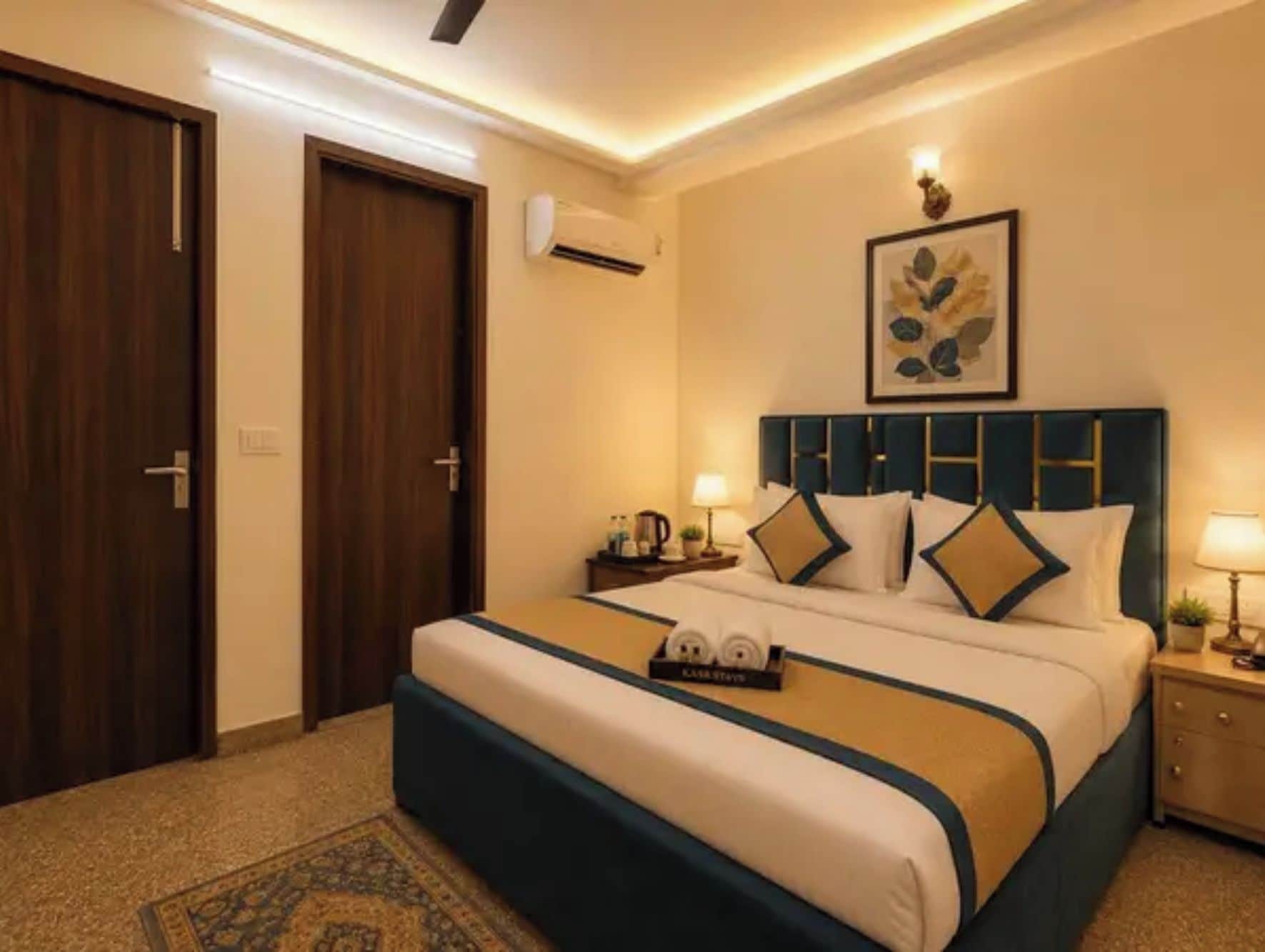 A hotel room with a large bed, a nightstand, a wall-mounted air conditioner, and a framed artwork above the bed.