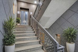 A staircase with a metal railing, potted plants on either side, and a textured wall. - FabHotel Premium Stay Ignou Road (New Delhi)