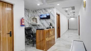 A reception area with a wooden desk labeled 'M Mauryan,' a black office chair, a mounted television, and a fire extinguisher.