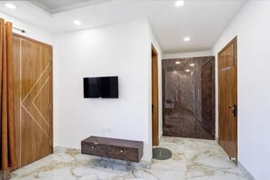 Una habitación con una televisión de pantalla plana montada en la pared, un mueble de madera debajo y un suelo con estampado de mármol.