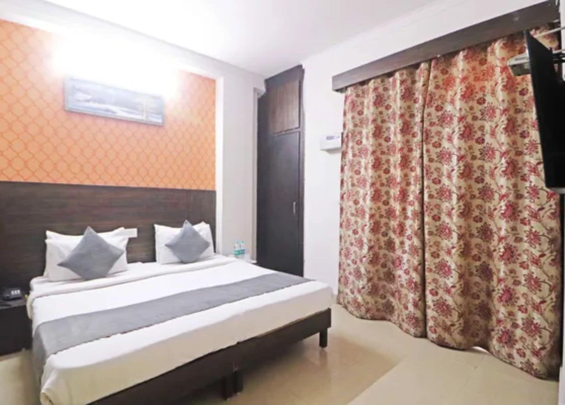 Habitación de hotel con cama, mesita de noche, cabecero, ventana con cortina y aire acondicionado de pared.