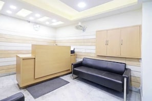 A reception area with a wooden desk, a black leather sofa, and a cabinet. - FabHotel Premium Stay Dasrathpuri (New Delhi)
