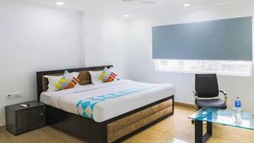 Een slaapkamer met een bed, nachtkastje, stoel, glazen tafel en een raam.