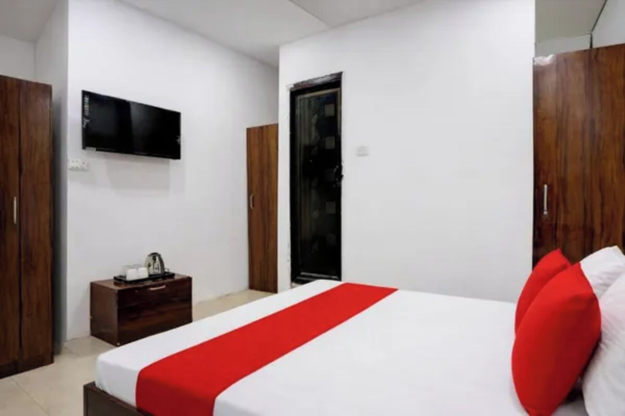 A hotel room with a bed, a television mounted on the wall, a wardrobe, and a small table with a kettle.