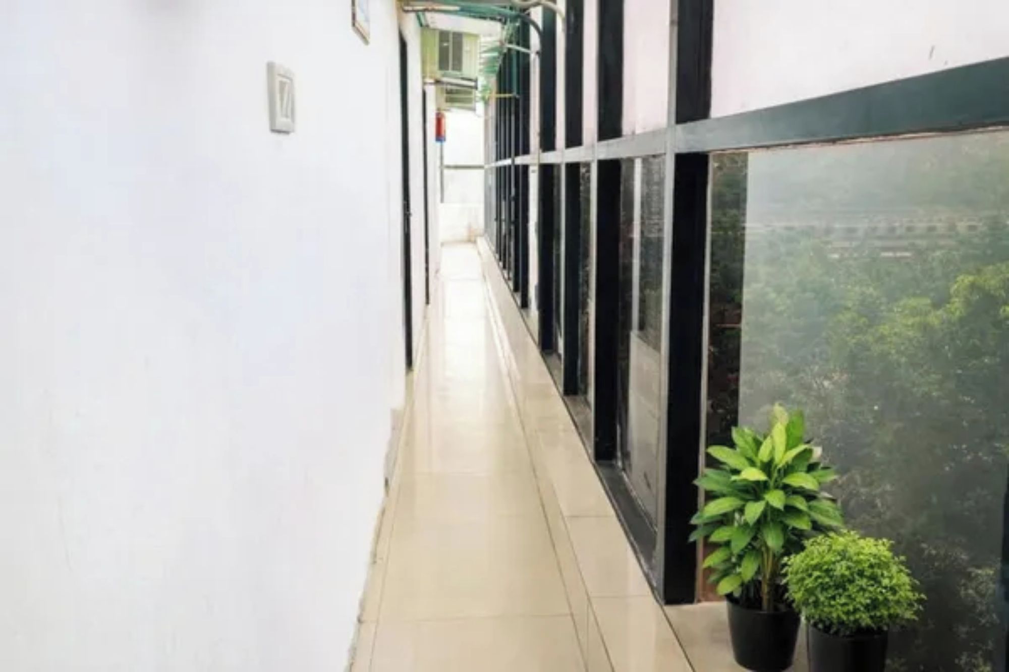 A corridor with a tiled floor, a potted plant, and a window with a view of greenery.