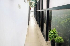 Un pasillo con piso de baldosas, una planta en maceta y un ventanal con vista a follaje.