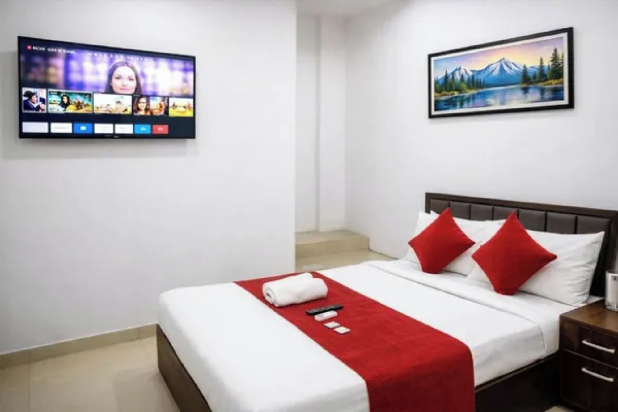 A hotel room with a bed, a TV mounted on the wall, and a painting above the bed.