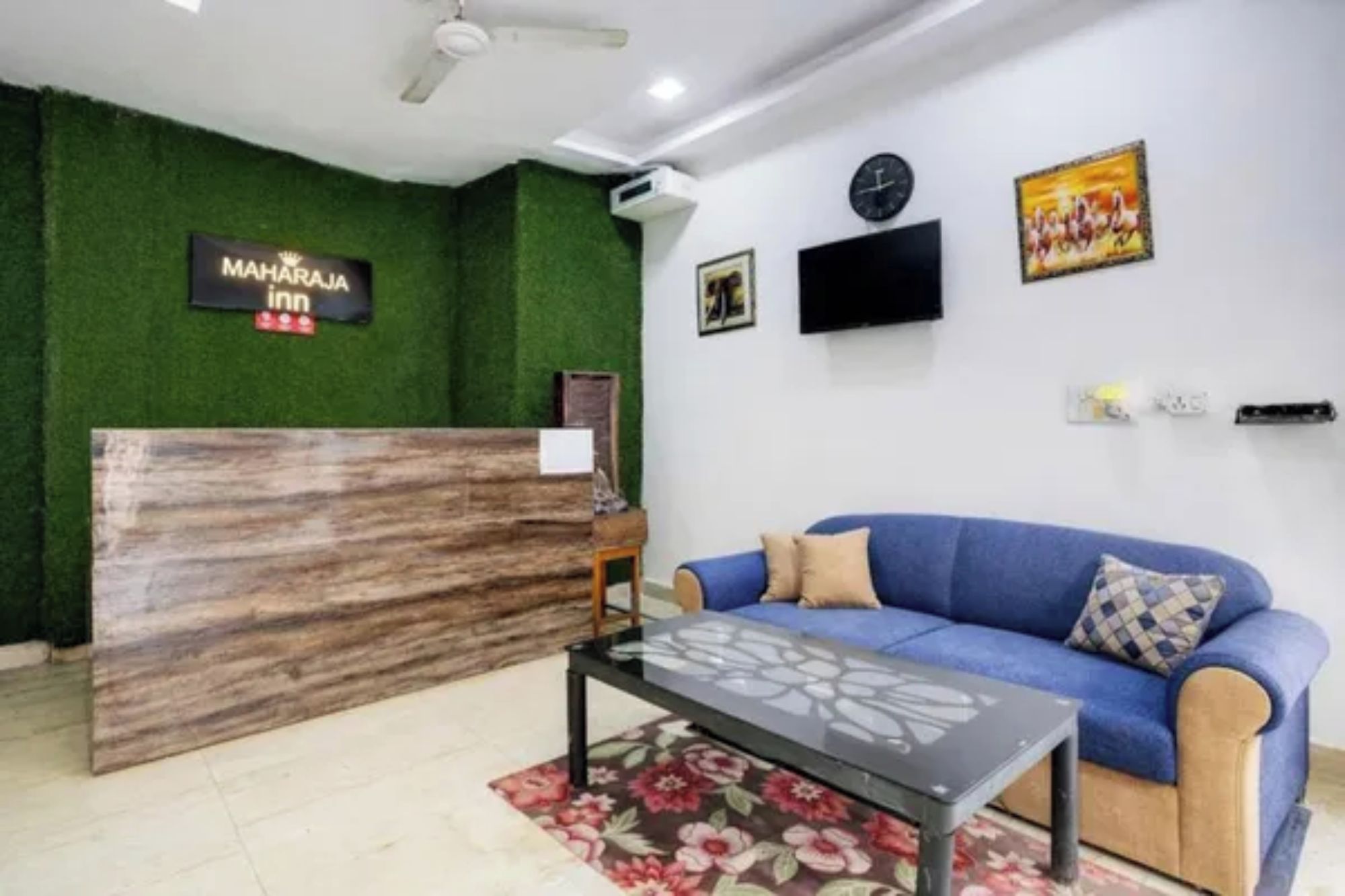 A reception area with a reception desk, a blue sofa, a clock, and a television on the wall.