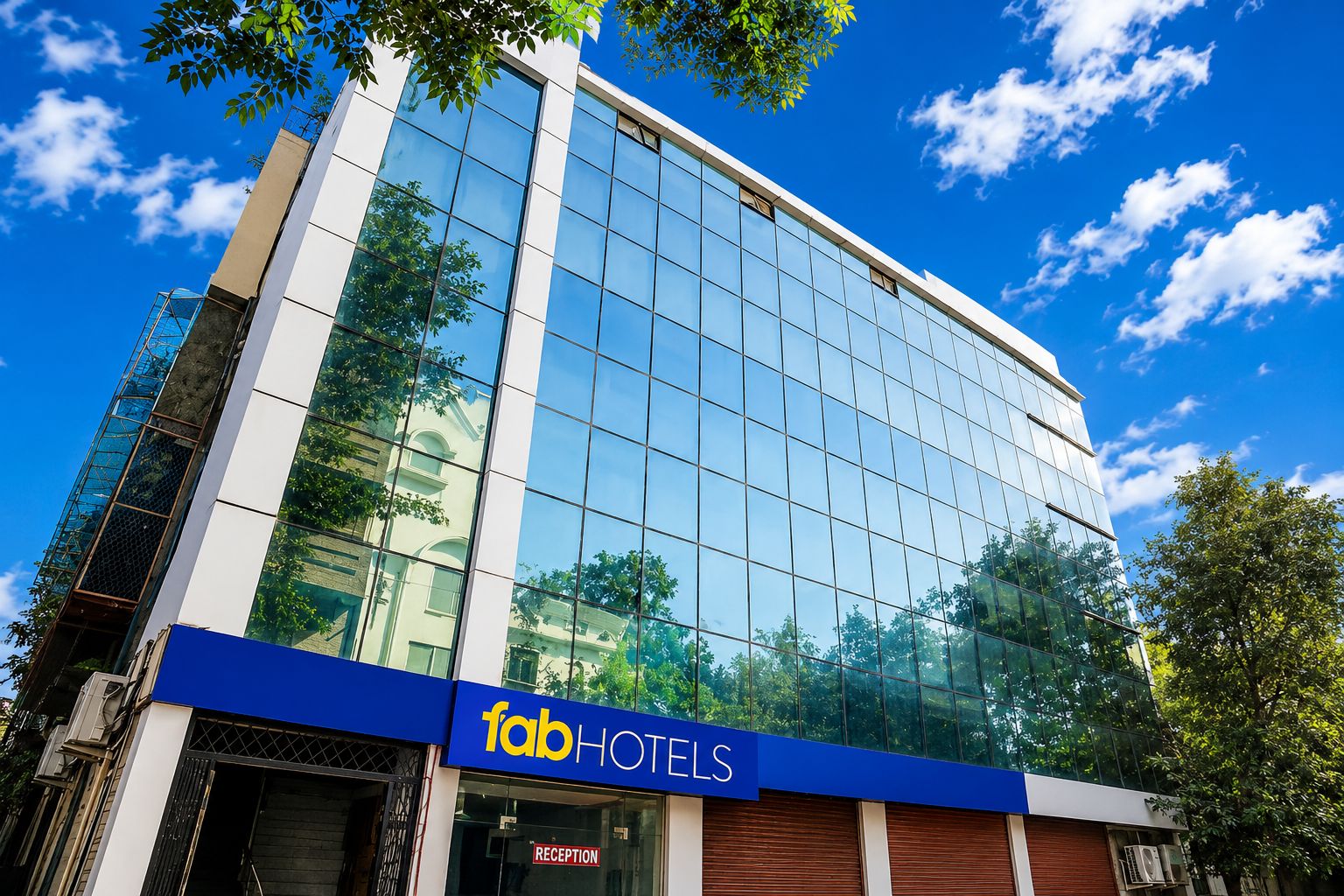 A modern hotel building with a glass facade, a reception area, and a blue sign indicating it's a Fab Hotels property.