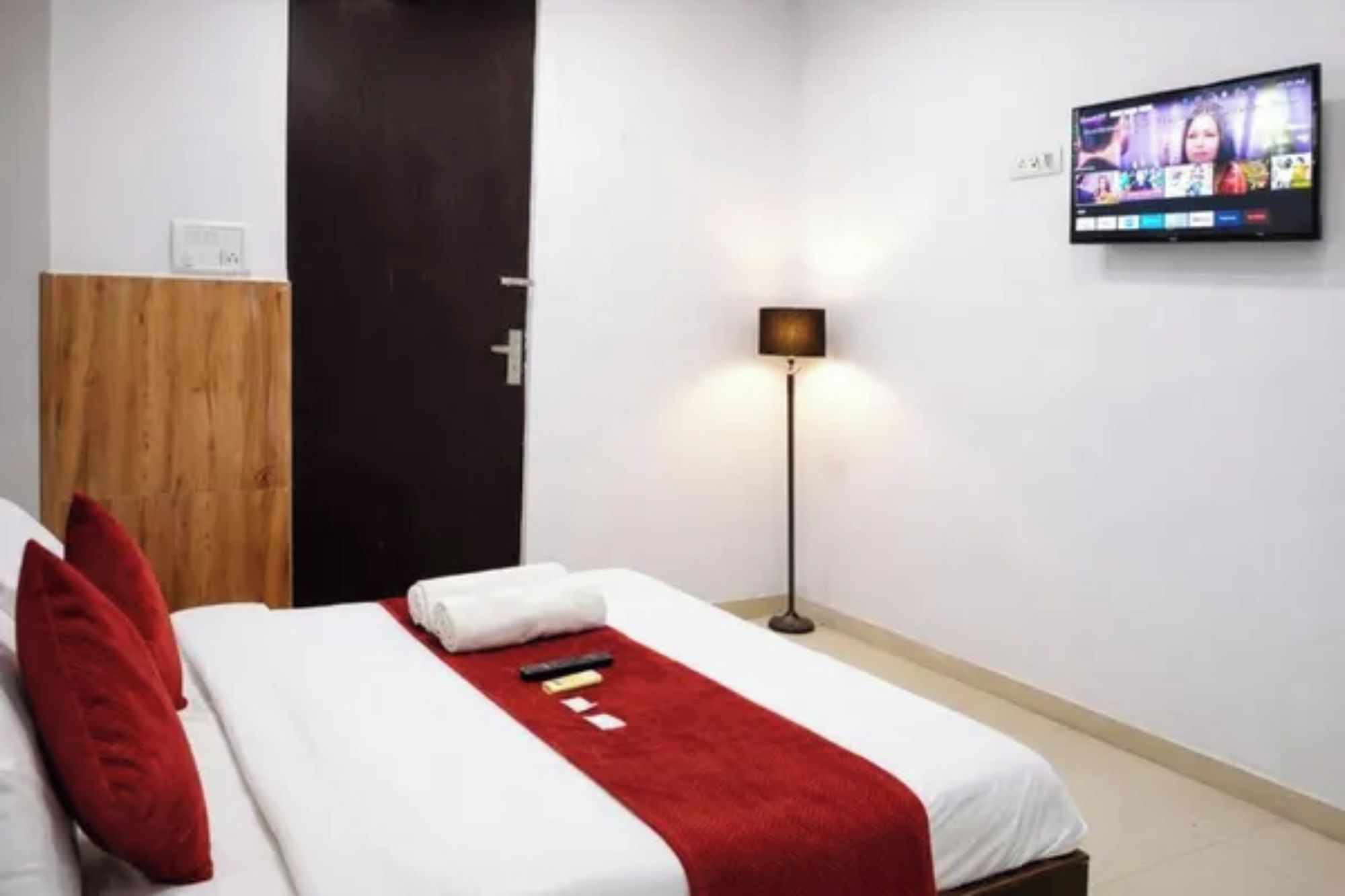 A hotel room with a bed, a TV mounted on the wall, and a floor lamp.