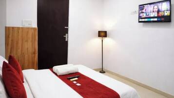 A hotel room with a bed, a TV mounted on the wall, and a floor lamp.