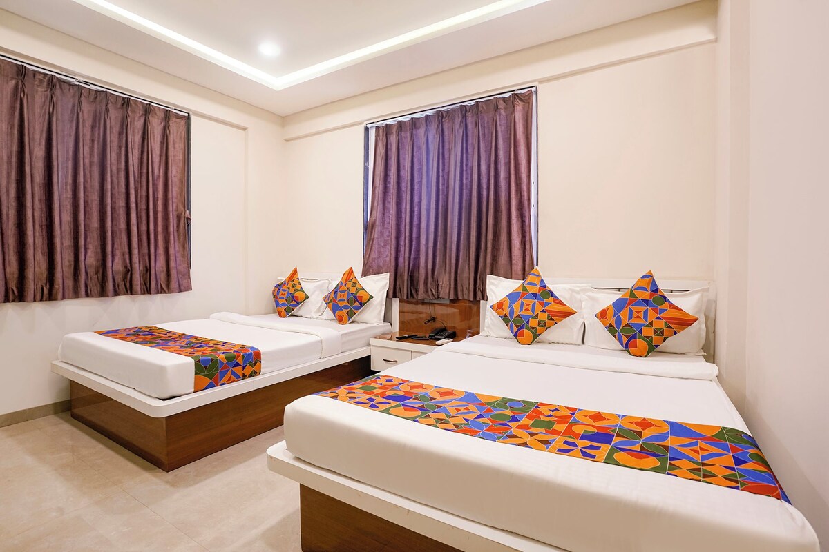 A hotel room with two beds, each with a patterned bedspread and pillows, a wooden headboard, and a large window with curtains.
