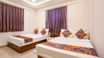 A hotel room with two beds, each with a patterned bedspread and pillows, a wooden headboard, and a large window with curtains.