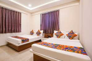 A hotel room with two beds, each with a patterned bedspread and pillows, a wooden headboard, and a large window with curtains. - FabHotel Royal Inn Regency (Pune)