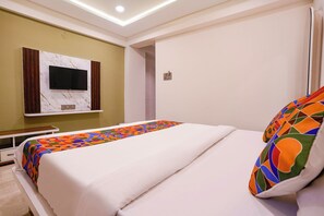 Quarto de hotel com cama, televisão fixada em parede de mármore e mesa de cabeceira.