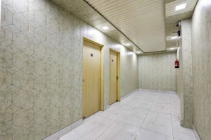 A hallway with hexagonal patterned walls, two wooden doors, and a tiled floor. - FabHotel Premium Villa Devli (New Delhi)