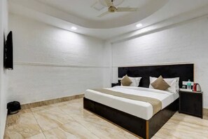 Una habitación de hotel con cama, mesita de noche, ventilador de techo y televisor montado en la pared.