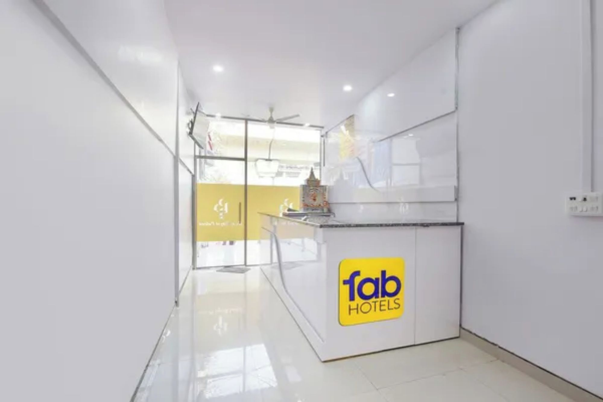 A hotel reception area with a glass partition, a ceiling fan, and a sign for 'fab hotels'.